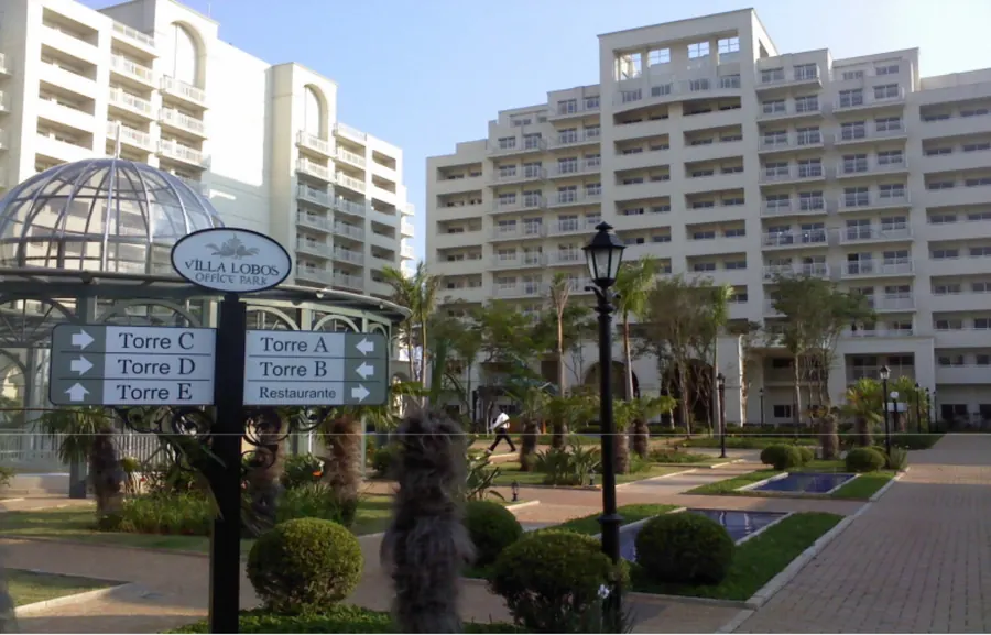Pátio ajardinado do Villa Lobos Office Park, com a placa de sinalização das torres A a E e do restaurante