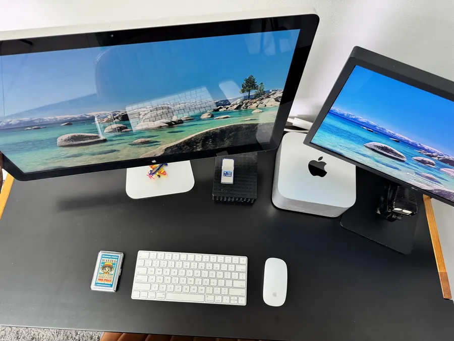Ilha de edição do Estúdio Gigante vista de cima: Mac mini, monitor Apple, segundo monitor, teclado e mouse sobre bancada preta