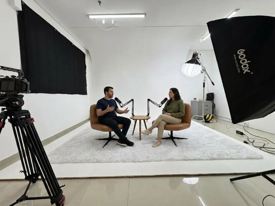 Gravação de podcast em dupla no ciclorama branco, com microfones em braço articulado e mesinha de apoio